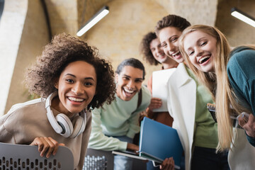 cheerful african american student with headphones looking at camera together with multicultural...