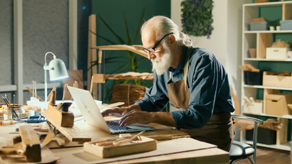 A Focused Carpenter Develops Layouts from Wood, Models 3D Sketches Using a Laptop in a Home...