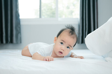 Cute little asian baby lying on bed with soft blanket indoors