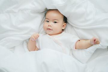 Cute little asian baby lying on bed with soft blanket indoors - Powered by Adobe