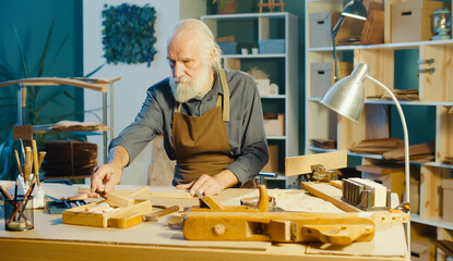 Professional Elderly Man Carpenter Working on Wood Using Carpentry Tools in the Garage. Craft Authentic Workshop. Handicraft, Creative Small Business. Profession, Art and Hobby Concept.