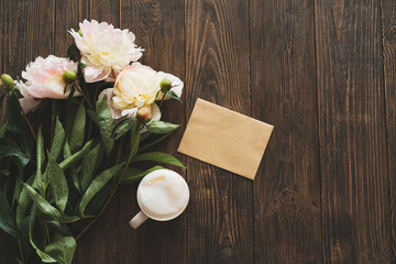 Obraz na płótnie Canvas Bouquet white pink peonies flowers, cup coffee and card on a wooden background. Flat lay minimalist aesthetic peonies. Beautiful card for Mother's Day or Women's Day