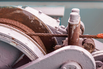 close-up of an old large winch with a rusty cable wound around it.