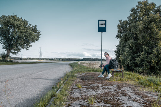 a woman sits on a bench at a city bus stop. Travel around the country.