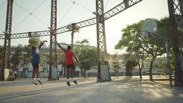 Cinematic footage of a street basketball game outdoor. Basketball players training and having fun at the court doing slam dunks and tricks