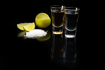 Tequila gold and silver in glasses, lime and salt. On a black background.