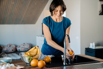 White mature woman washing fruits while cooking in kitchen