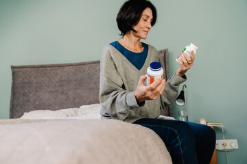 White mature woman examining medicine while sitting on bed