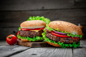 Two delicious homemade burgers of beef on an old wooden table. Fat unhealthy food close-up.