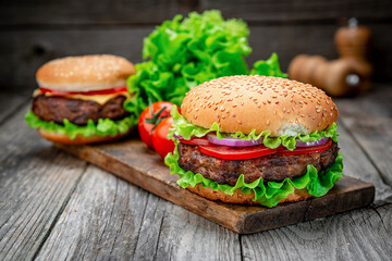 Two delicious homemade burgers of beef on an old wooden table. Fat unhealthy food close-up.