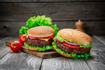 Two delicious homemade burgers of beef on an old wooden table. Fat unhealthy food close-up.