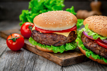 Two delicious homemade burgers of beef on an old wooden table. Fat unhealthy food close-up.
