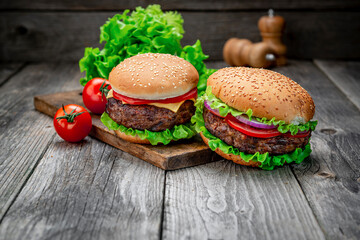 Two delicious homemade burgers of beef on an old wooden table. Fat unhealthy food close-up.