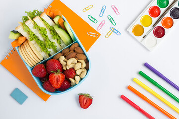 School lunch in the blue box and school stationery on the white background. Top view. Copy space.