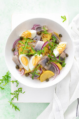 Herring and boiled potato salad with egg, capers and red onion. Top view