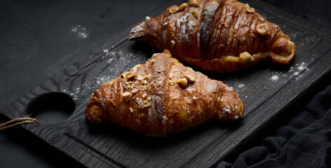 baked croissant on a wooden board and sprinkled with powdered sugar, black table. Appetizing pastries for breakfast