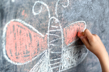 The child's hand draws a butterfly with pink wings with chalk on the blackboard