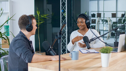 Female Host Talking to a Guest Friend on a Podcast Radio Station in the Studio. African American...