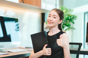 Portrait of successful and smiling young business woman holding file feeling confident and proud while standing in office and looking at camera