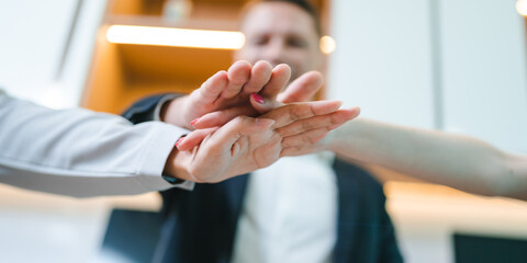 Team of young male and female employees stacking hands on top of each others to depict unity and harmony amongst colleagues for project and positive work environment