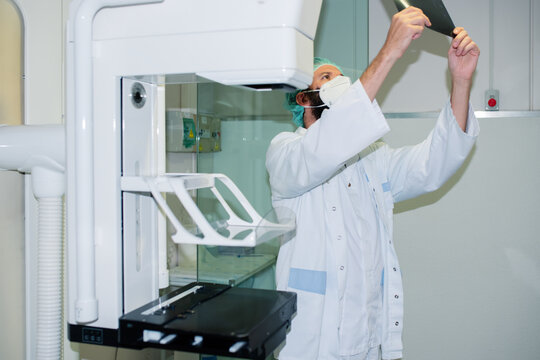 Doctor with mask checking mammography of woman in x-ray room.