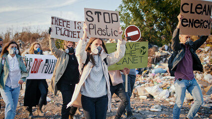 Young Generation Care About the Future. Group of Young Volunteers in Gas Masks With a Poster Calling to Take Care of the Environment While Going Trough at Garbage Dump.