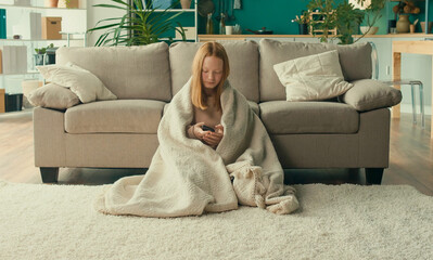 A Depressed Red Haired Teenage Girl Covers Herself with a Blanket in Her Living Room at Home. A Sad Teenager Feels Anxiety, Stress, Shame, Fear. Teenage Psychological Trauma, Mocking. Mental Health.