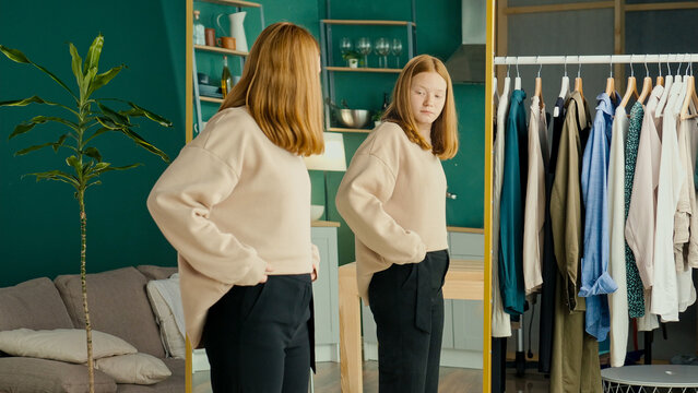 Depressed Red haired Teenage Girl Looking at Her Reflection in the Mirror. Unhappy, Dissatisfied, Insecure Teenager. Concept of Eating Disorder, Anorexia, Bulimia. Mental Health.
