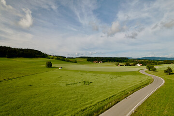 Naklejka premium Aerial view of rural landscape with winding country road at village of Forch, Canton Zürich, on a blue cloudy summer morning. on a Photo taken June 8th, 2022, Forch, Switzerland.