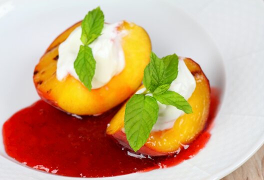 Grilled peaches with mascarpone and strawberry jam on white plate.  Decorated with young leaves of fresh mint.