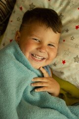 Top view portrait of happy smiling toddler boy lying on bed and laughing in the camera. Concept of happy children having good time at home.
