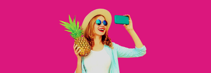 Summer portrait of happy smiling woman with pineapple taking selfie by smartphone wearing straw hat, sunglasses on pink background