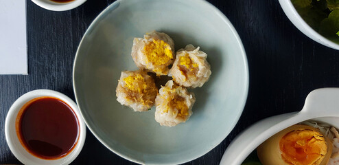 Top view of four steamed dumplings on green dish with sliced boiled egg and sweet sauce. Chinese food with fried garlic topping. Flat lay of Asian snack and Famous food in Asia