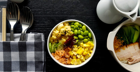 Flat lay of fresh salad with sliced of corn, salmon, green nut or bean,  pineapple, bacon, cucumber and topping with white and black sesame. Set of Healthy food  with spoon and fork put in napkin. 