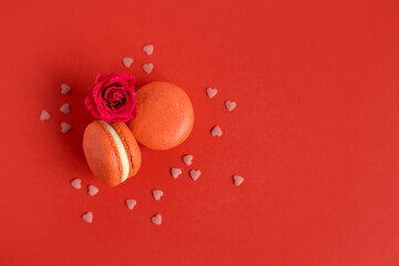 Tasty french macarons with rose flower on a red background.