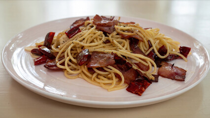 Selective focus, spagetti aglio olio with bacon with lots of dried chilli on white plate.