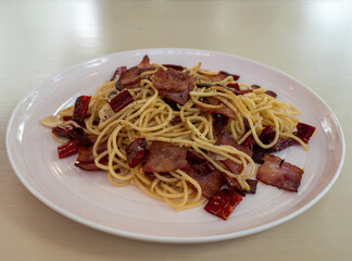 Selective focus, spagetti aglio olio with bacon and lots of dried chilli on white plate. Homemade style pasta.