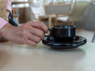 Fototapeta na wymiar Close up female hand holding black color coffee cup in the coffee shop.