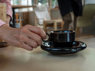 Close up female hand holding black color coffee cup in the coffee shop.