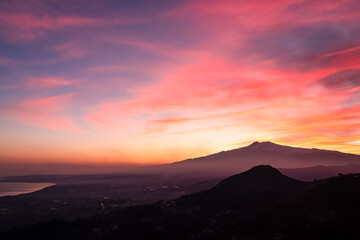 Panoramic view on silhouette of hills during twilight. Watching beautiful sunset behind volcano Mount Etna near Castelmola, Taormina, Sicily, Italy, Europe, EU. Clouds with vibrant red orange colors