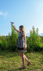 Full length portrait of a happy girl in grey dress holding up a paper plane into the blue sky and dreams of flying