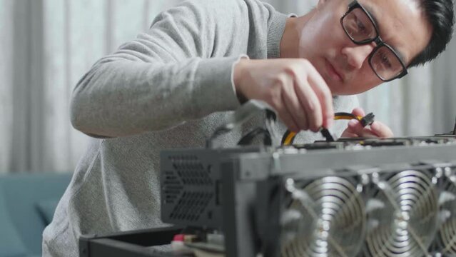 Close Up Of Asian Man Wearing Glasses Connects The Power Cords Of Mining Rig For Mining Cryptocurrency
