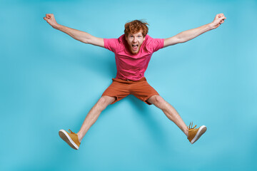 Obraz premium Cheerful young redhead man jumping against blue background