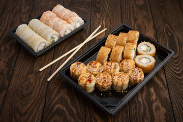Oriental cuisine, rolls in plastic take-out trays on a wooden table close up