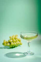 Wine Glass of white wine and grapes with bright shadows over green background