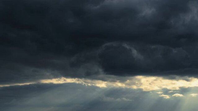 bright sunlight through a dark dramatic sky with thunderclouds, extreme weather, timelapse
