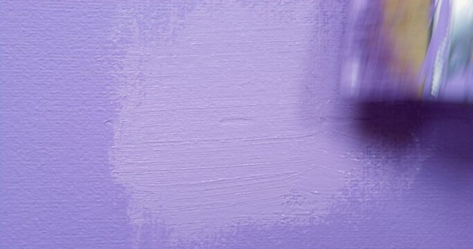 Person uses wooden brush for painting wall in light purple color. Paint equipment for making renovation in new apartment extreme closeup