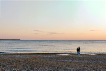 Fototapeta na wymiar Coppia in lontananza controluce al tramonto sulla spiaggia di fronte al mare