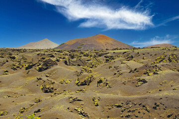 Beautiful barren dry landscape,  black jagged lava sand field, red volcano  cone, clear blue summer sky - Timanfaya NP, Lanzarote