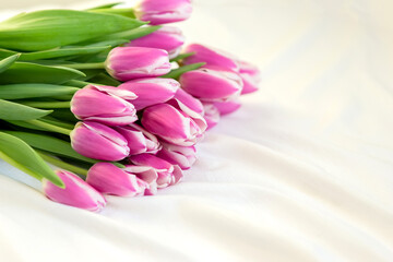 A bouquet of beautiful pink tulips lies on a white bed. copy space